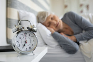 senior woman sleeping with close-up of alarm clock